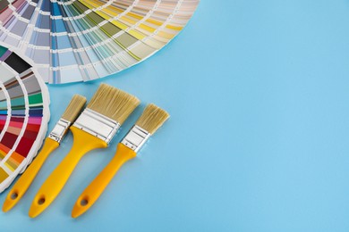 Photo of Color selection charts and paint brushes on light blue table, space for text. Decorating and design