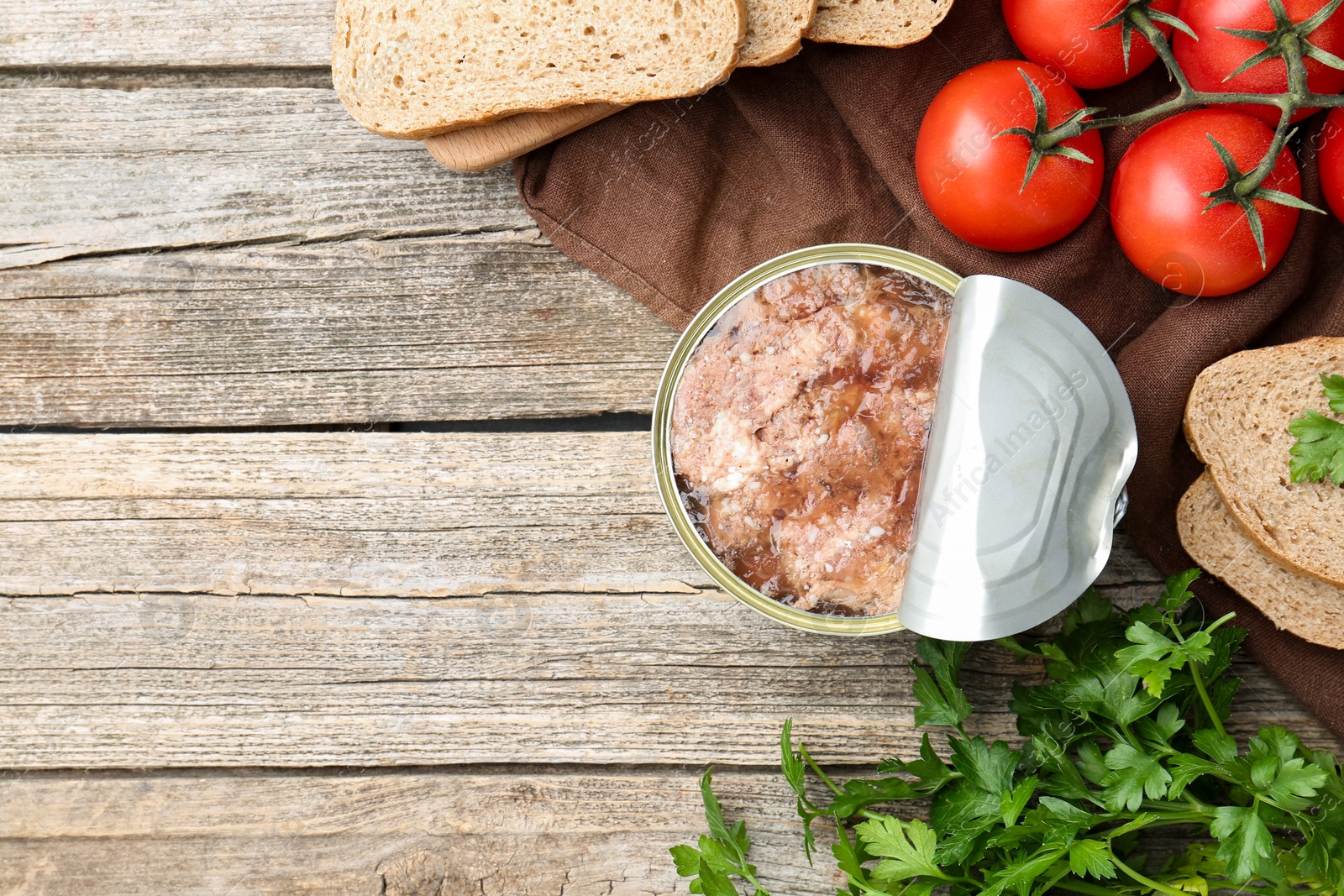 Photo of Canned meat in tin can served on wooden table, flat lay. Space for text