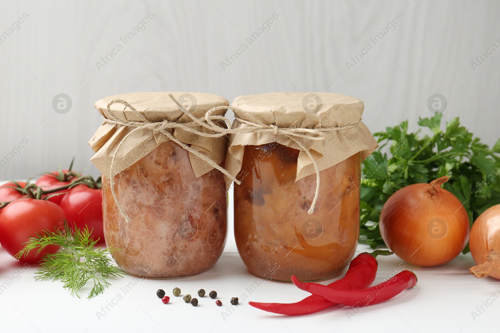 Photo of Canned meat in glass jars and fresh products on white wooden table