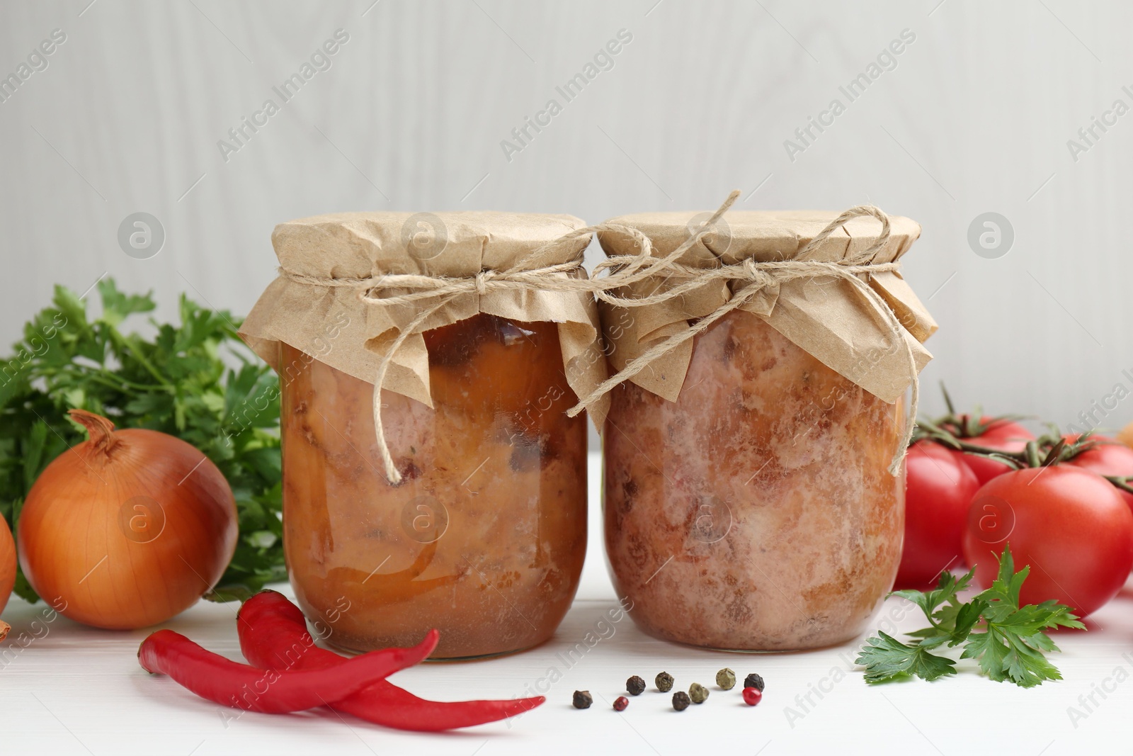 Photo of Canned meat in glass jars and fresh products on white wooden table