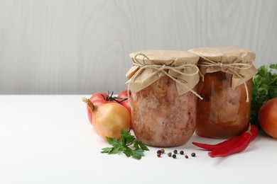 Photo of Canned meat in glass jars and fresh products on white wooden table, space for text