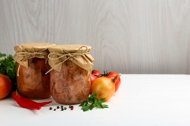 Photo of Canned meat in glass jars and fresh products on white wooden table, space for text