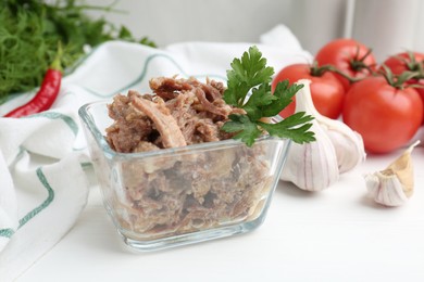 Photo of Canned meat with parsley in bowl and fresh vegetables on white wooden table, closeup