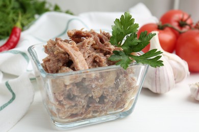 Photo of Canned meat with parsley in bowl on white table, closeup