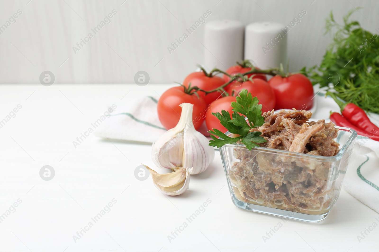 Photo of Canned meat with parsley in bowl and fresh vegetables on white wooden table, space for text