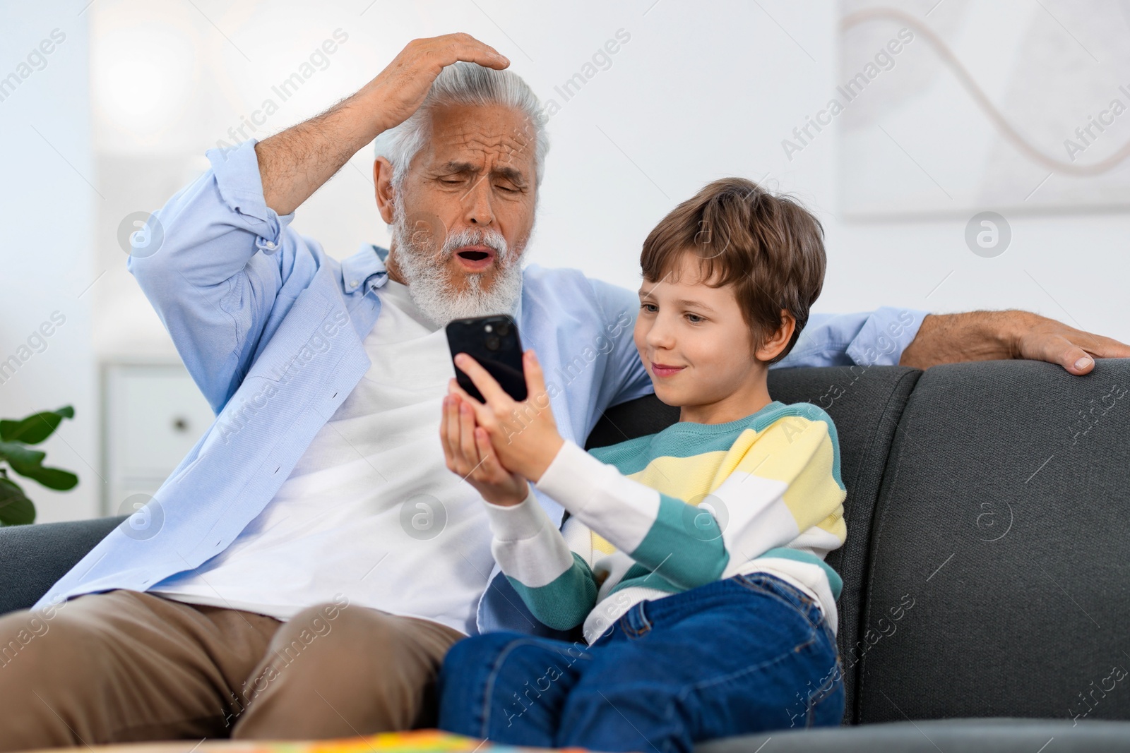 Photo of Grandpa and his grandson watching something on smartphone at home