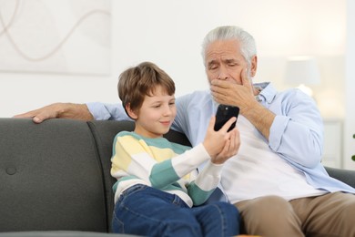 Photo of Grandpa and his grandson watching something on smartphone at home