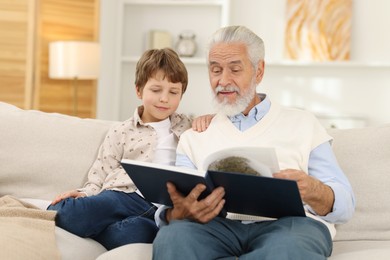 Grandpa and his grandson reading book together on sofa at home