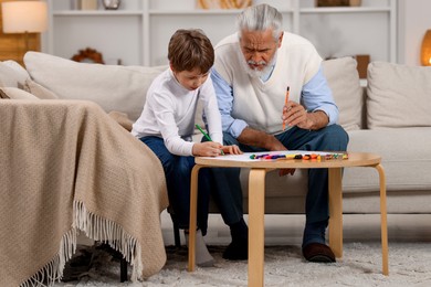 Grandpa and his grandson drawing at table indoors