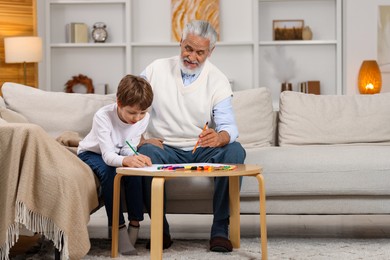 Photo of Grandpa and his grandson drawing at table indoors