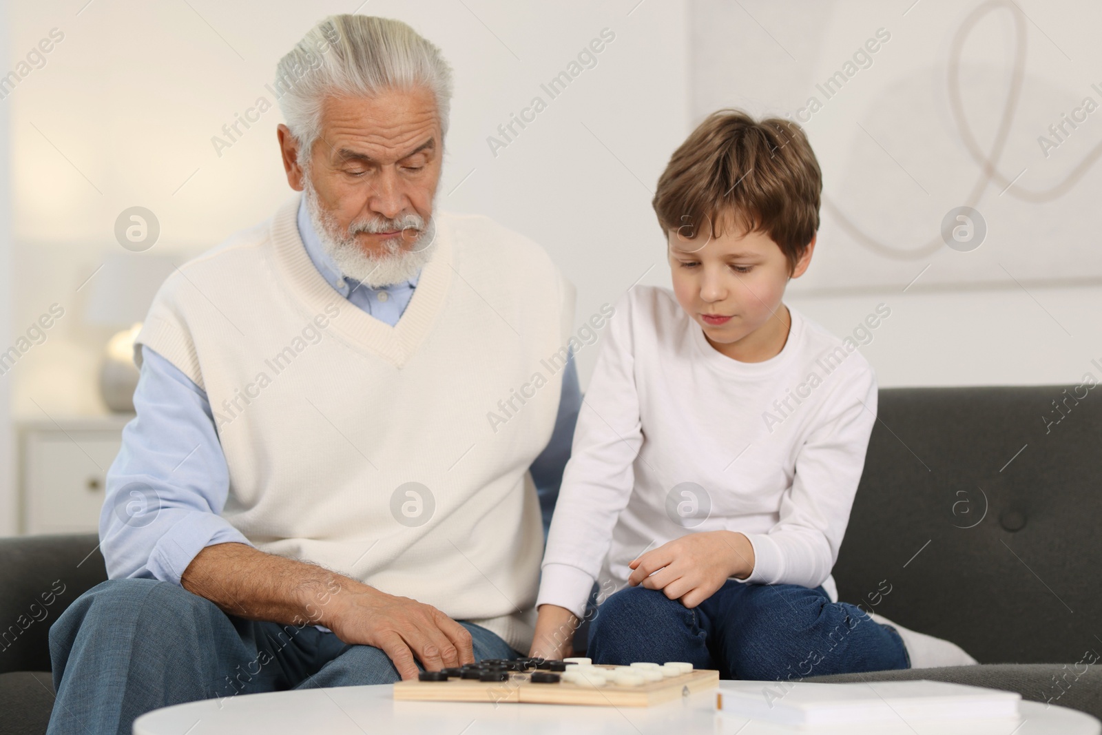 Photo of Grandpa and his grandson playing checkers at table indoors