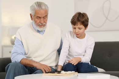 Photo of Grandpa and his grandson playing checkers at table indoors