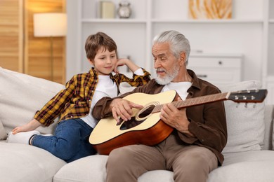 Photo of Grandpa teaching his grandson to play guitar on sofa at home