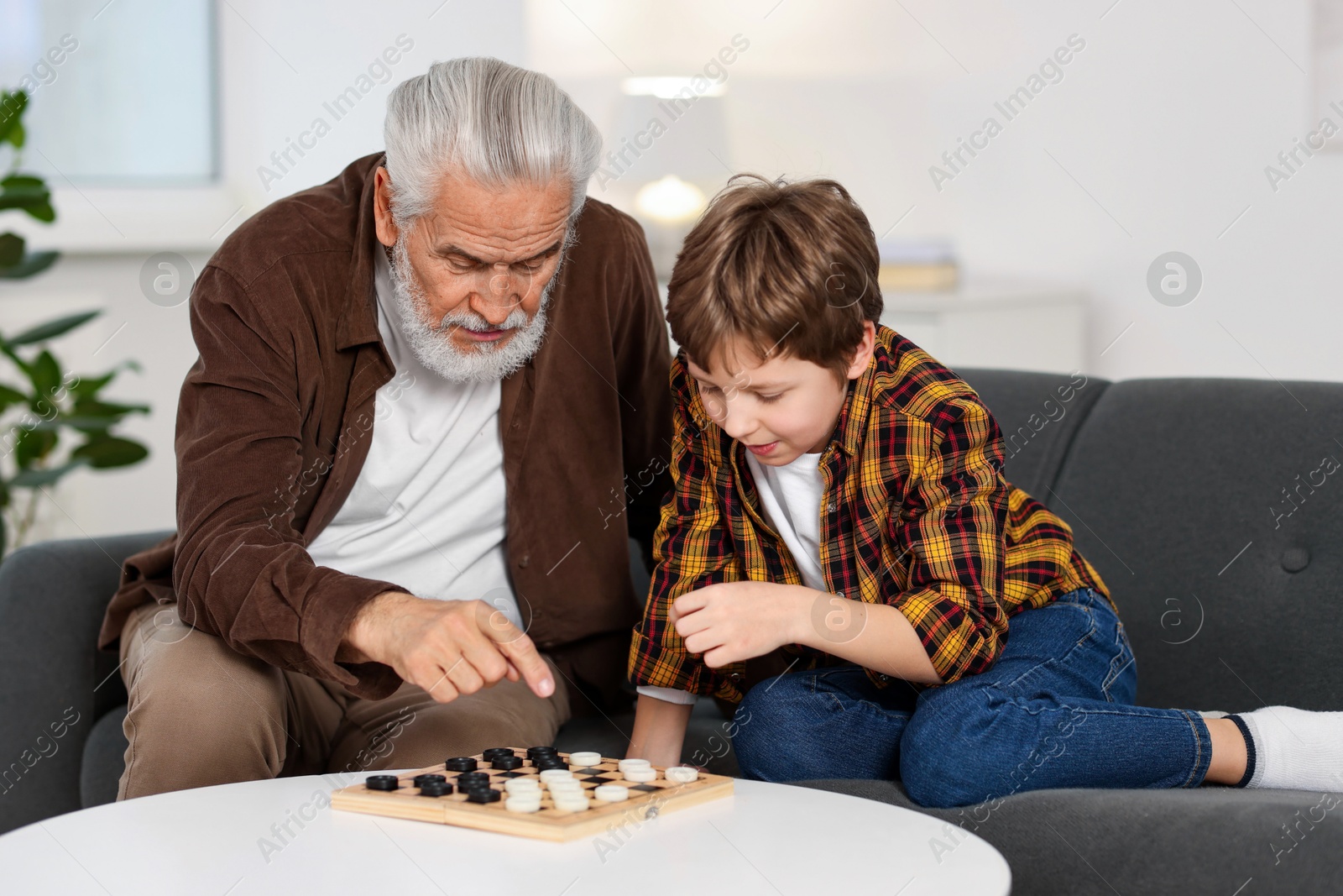 Photo of Grandpa and his grandson playing checkers at table indoors