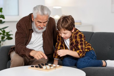 Grandpa and his grandson playing checkers at table indoors