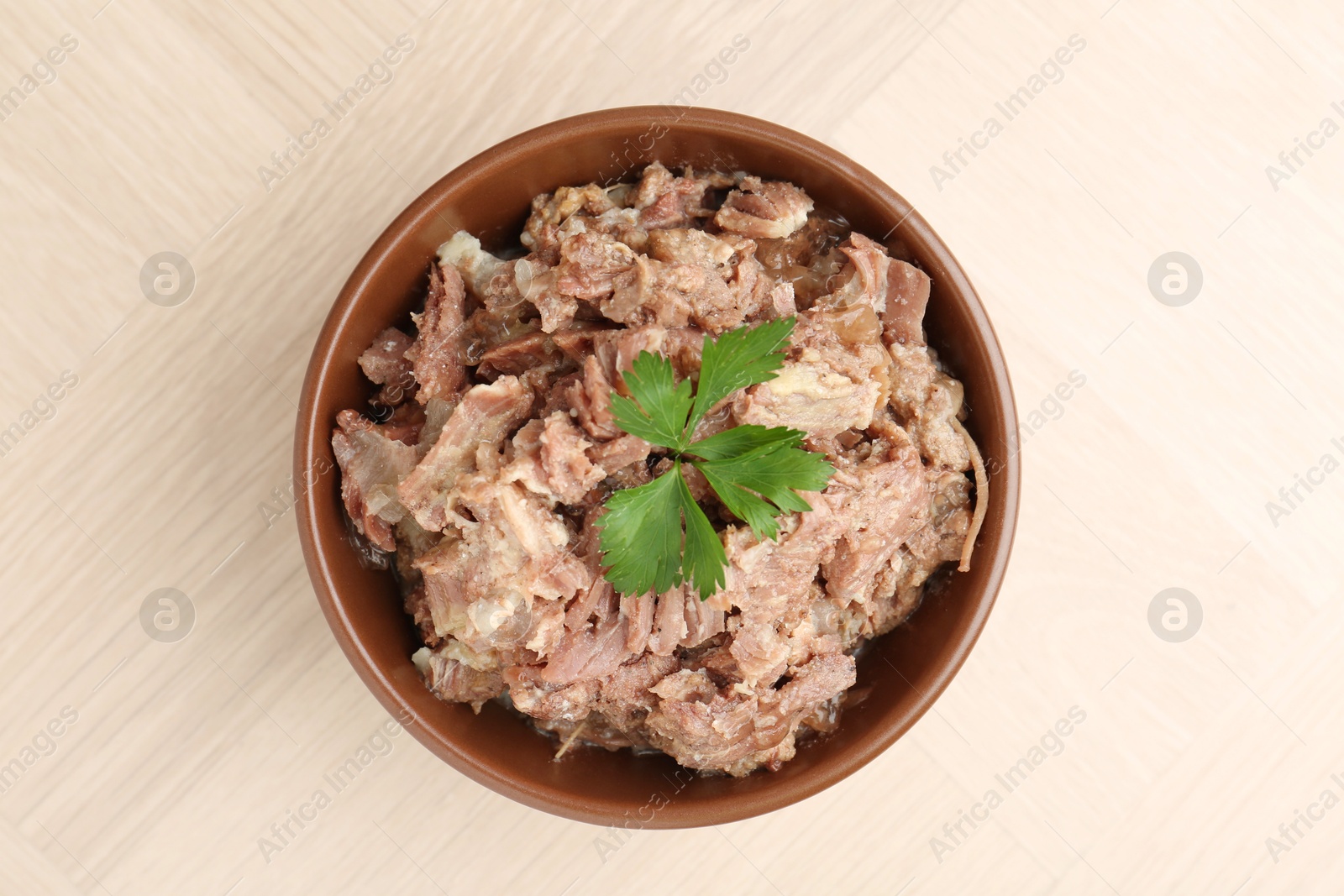 Photo of Canned meat with parsley in bowl on wooden table, top view