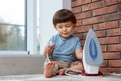 Little boy playing with iron plug near electrical socket at home. Child in danger