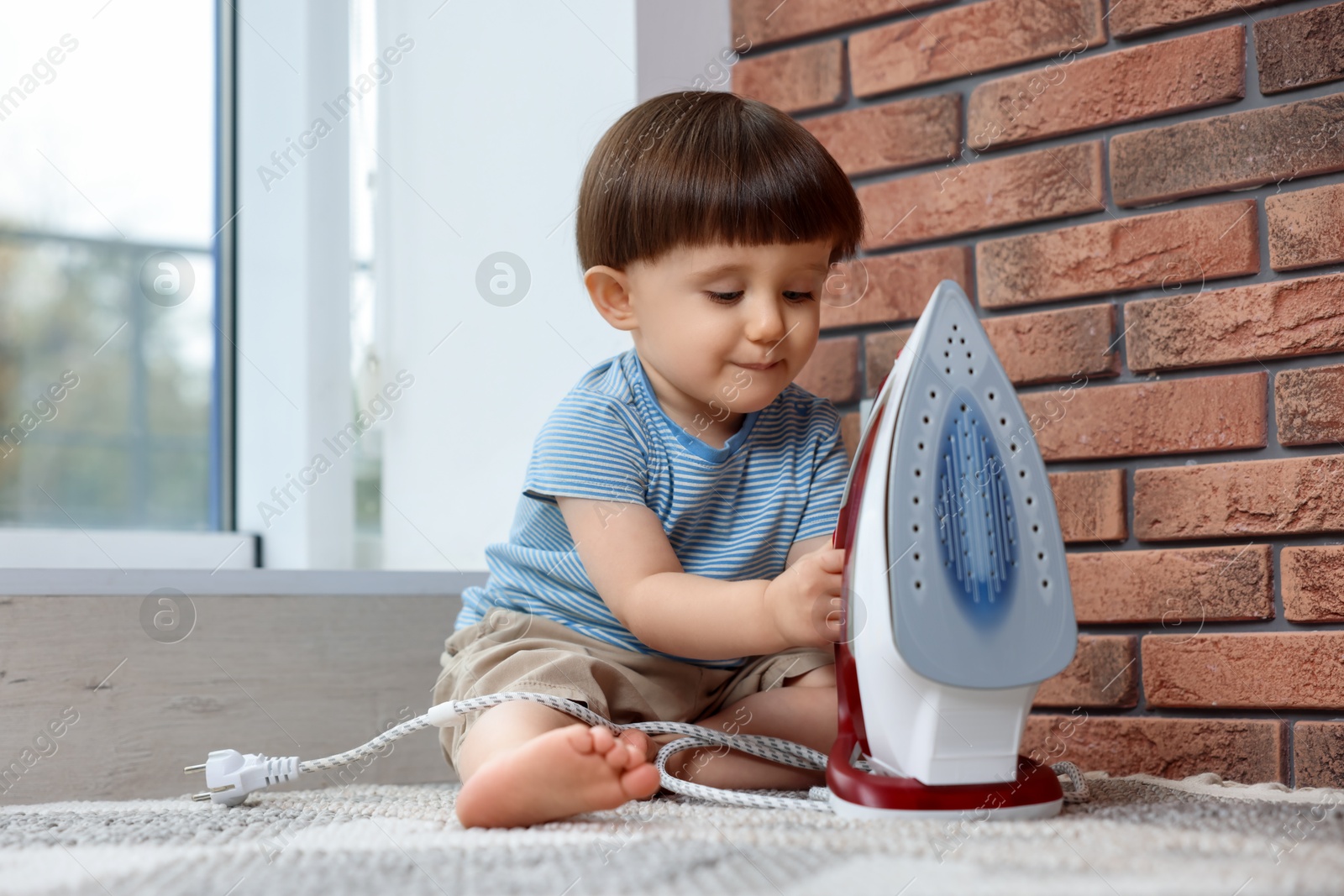 Photo of Little boy playing with iron at home. Child in danger