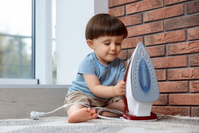 Little boy playing with iron at home. Child in danger