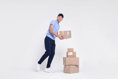 Happy postman with stack of parcels on white background