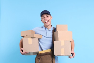 Happy postman with bag and parcels on light blue background. Space for text