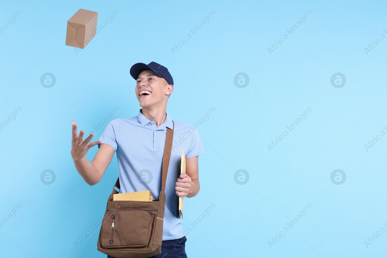 Photo of Happy postman with bag, envelopes and parcel on light blue background. Space for text