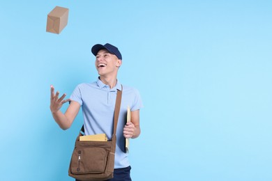 Happy postman with bag, envelopes and parcel on light blue background. Space for text