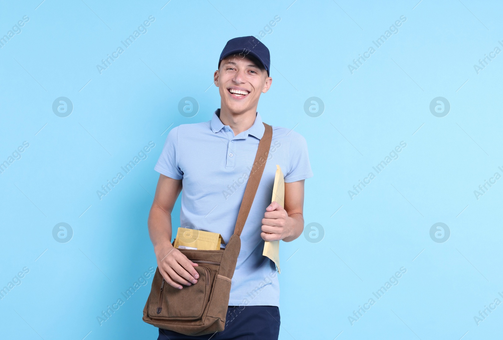 Photo of Happy postman with bag and envelopes on light blue background. Space for text