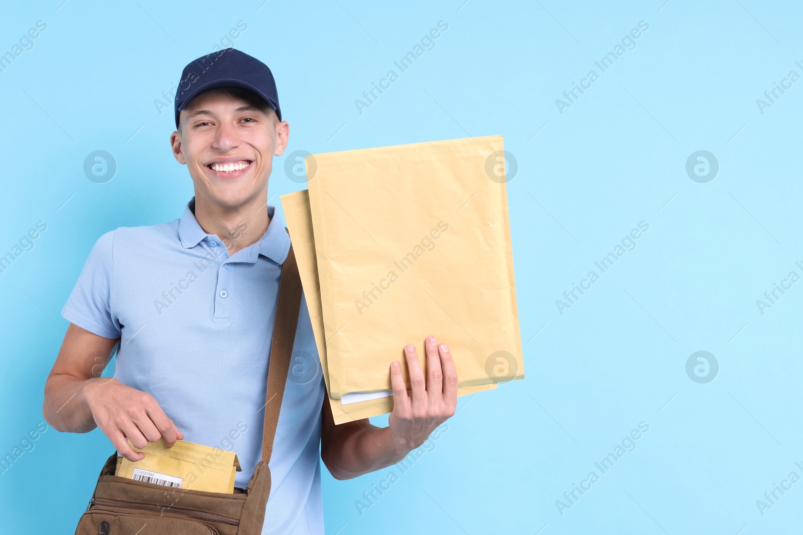 Photo of Happy postman with bag and envelopes on light blue background