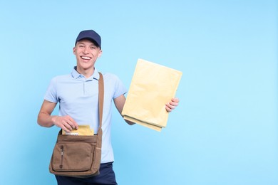 Photo of Happy postman with bag and envelopes on light blue background. Space for text