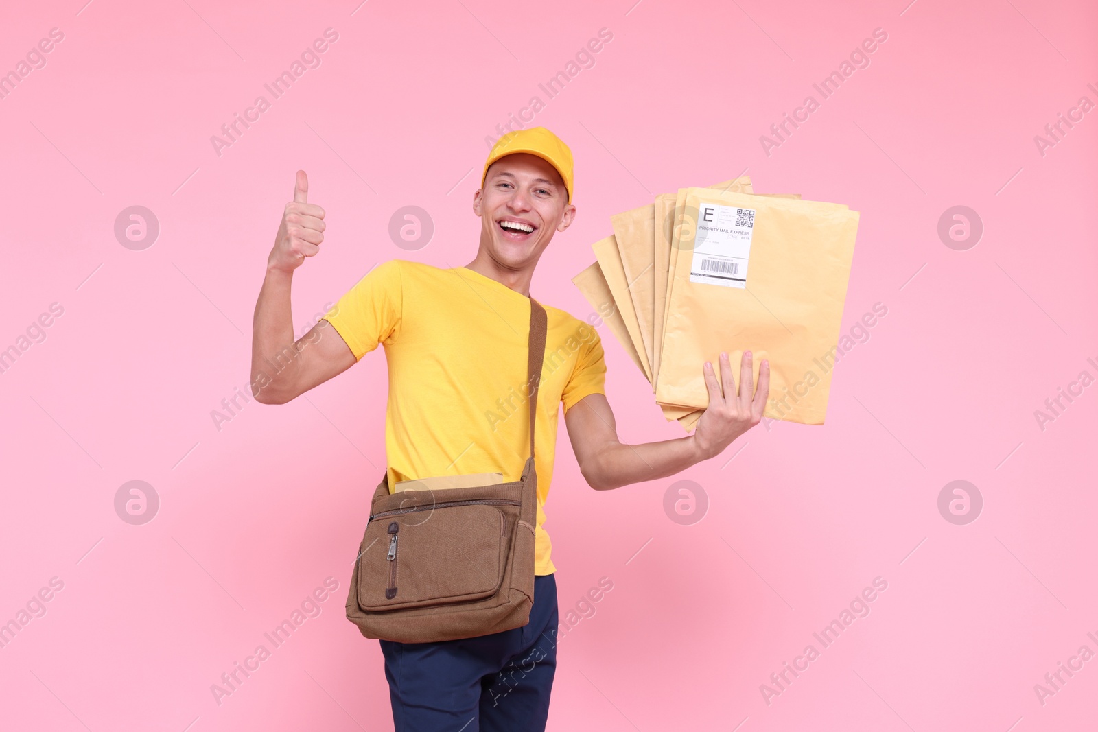 Photo of Happy postman with bag and envelopes showing thumbs up on pink background