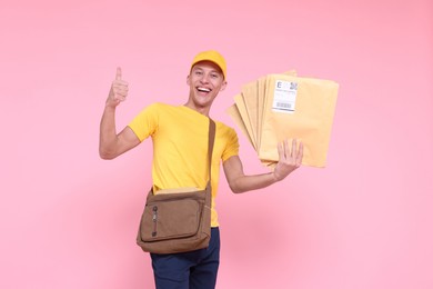 Happy postman with bag and envelopes showing thumbs up on pink background