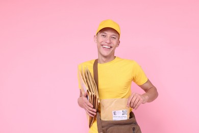 Happy postman with bag and envelopes on pink background