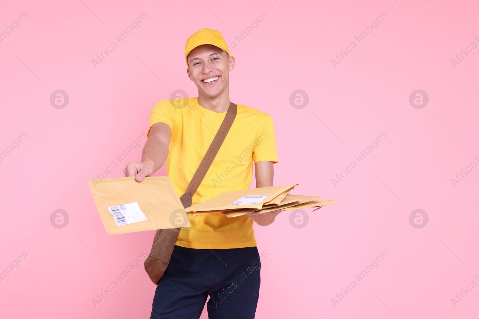 Photo of Happy postman with bag giving envelopes on pink background. Space for text