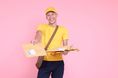 Photo of Happy postman with bag giving envelopes on pink background. Space for text