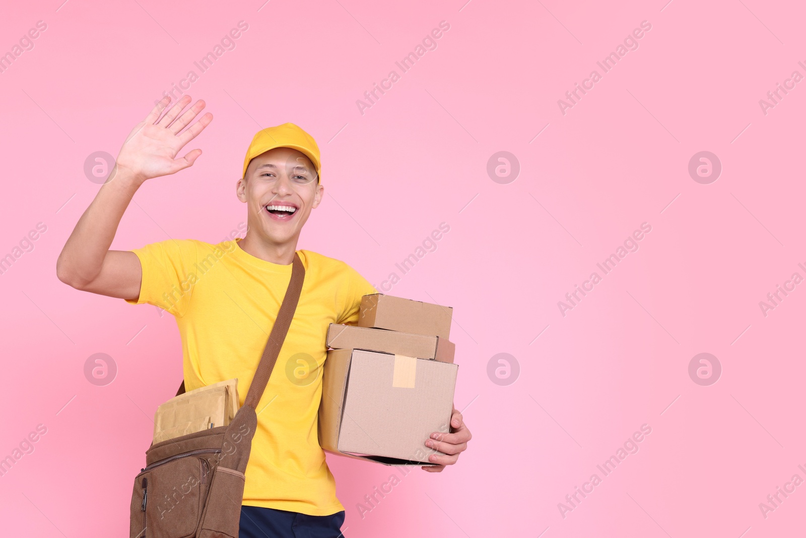 Photo of Happy postman with parcels waving hello on pink background. Space for text