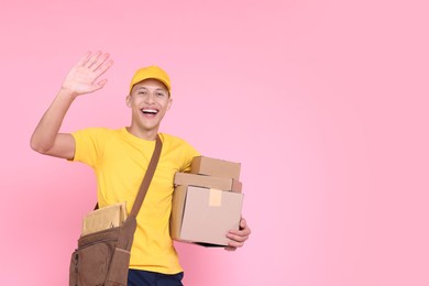 Happy postman with parcels waving hello on pink background. Space for text