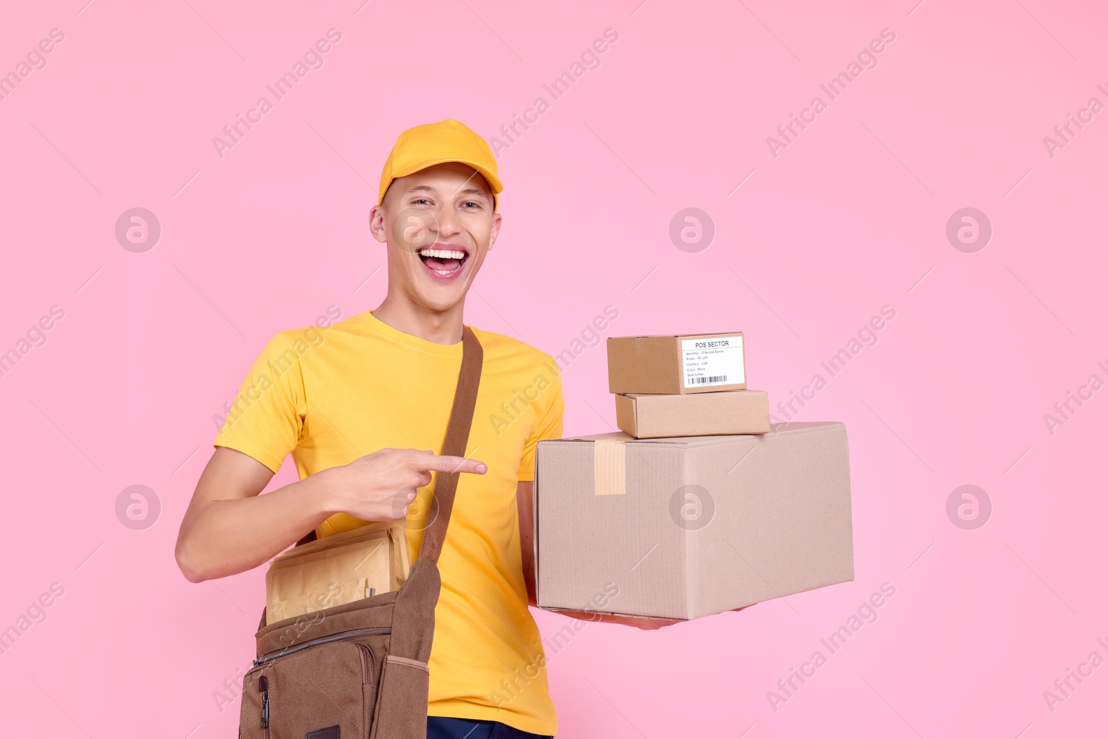 Photo of Happy postman pointing at parcels on pink background