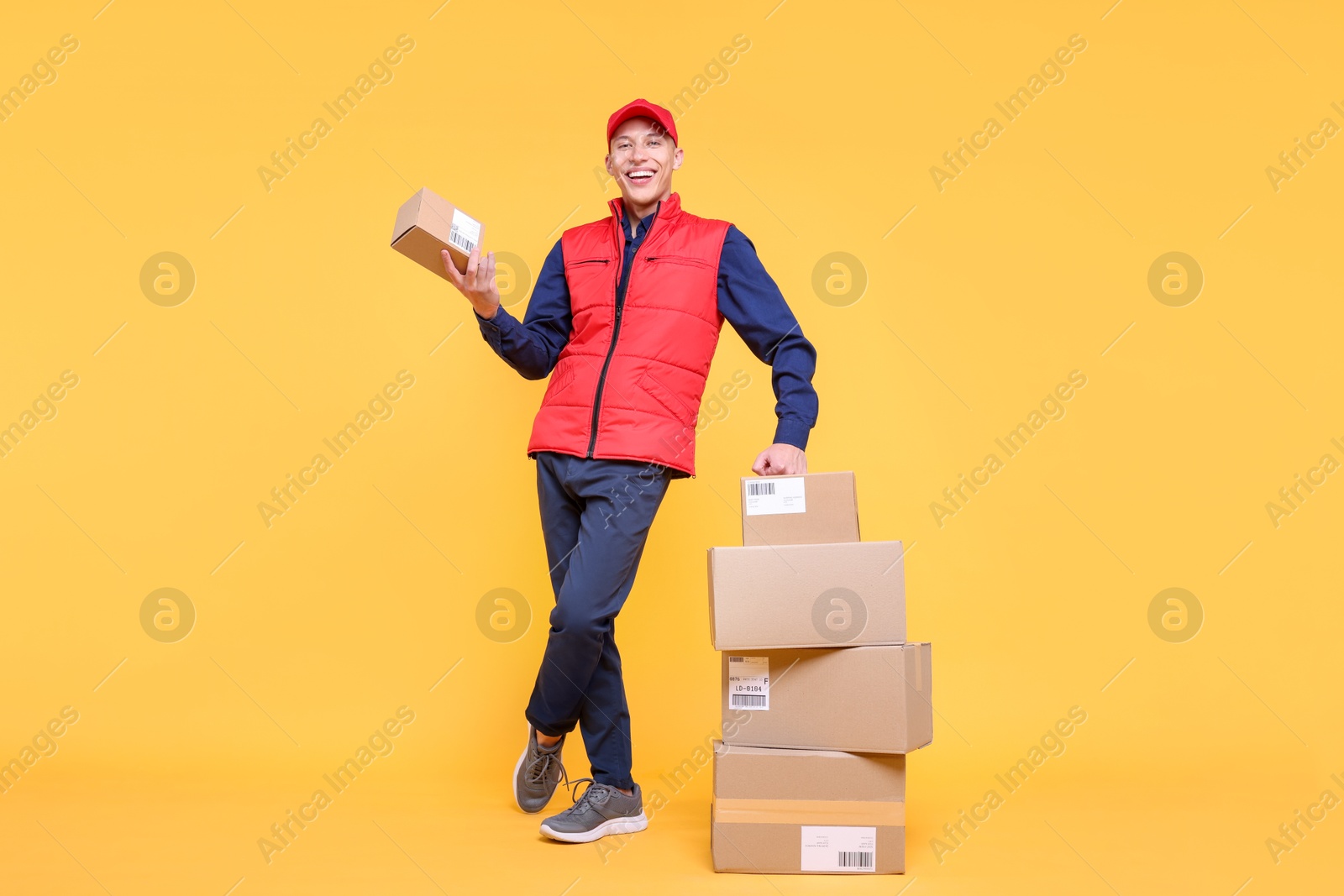 Photo of Happy postman with parcels on yellow background