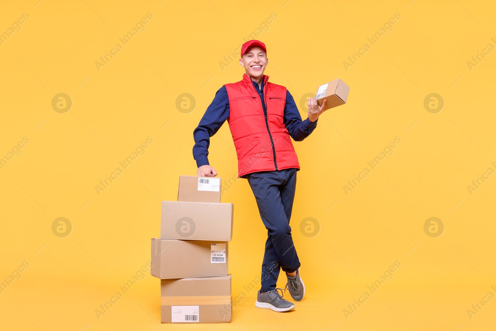 Photo of Happy postman with parcels on yellow background