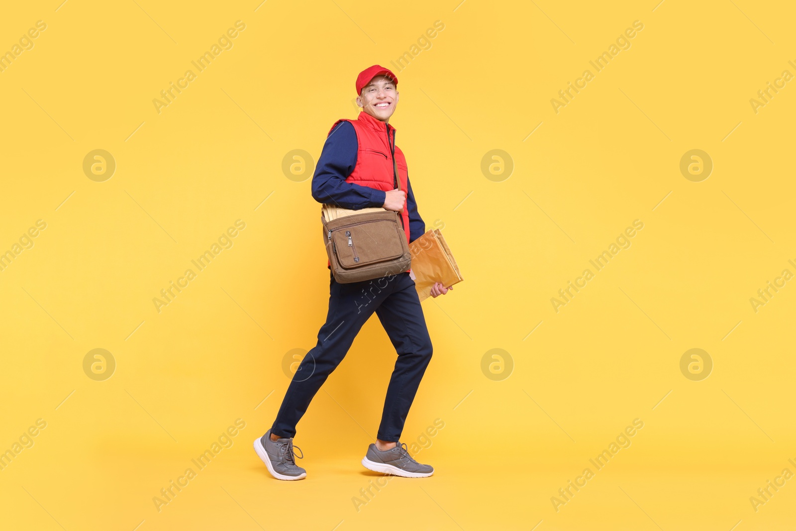 Photo of Happy postman with bag and envelopes on yellow background