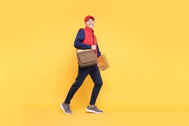 Happy postman with bag and envelopes on yellow background