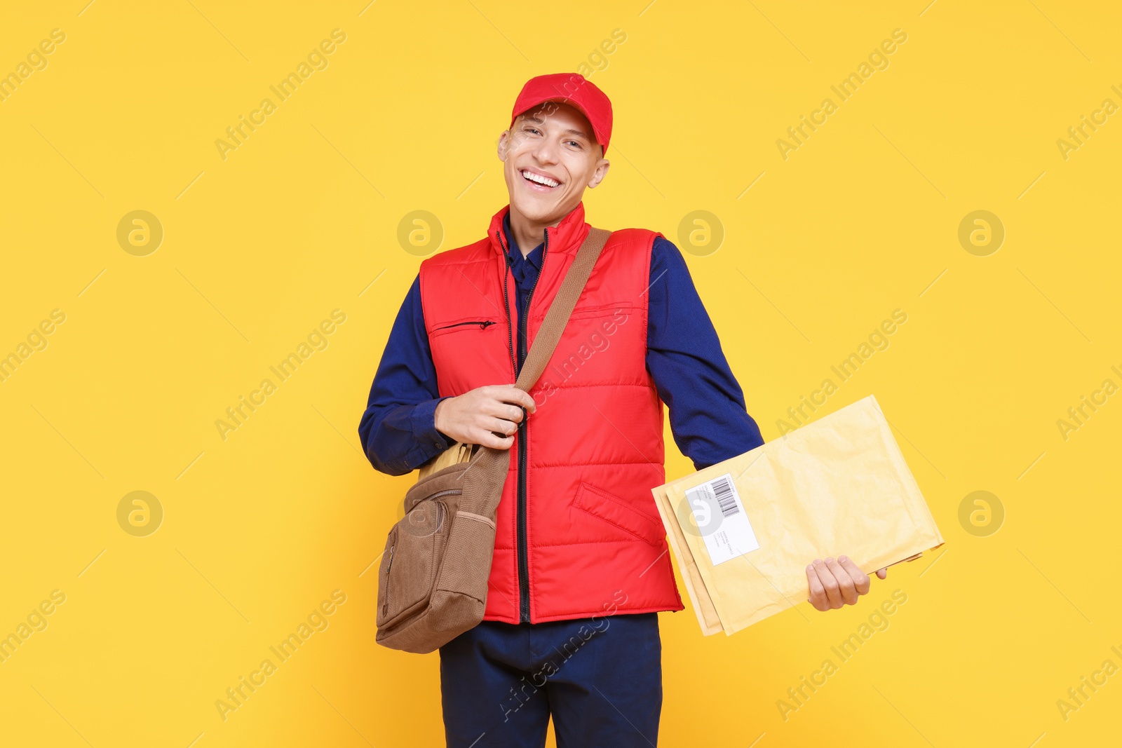 Photo of Happy postman with bag and envelopes on yellow background