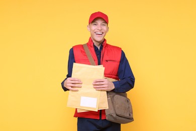 Photo of Happy postman with bag and envelopes on yellow background