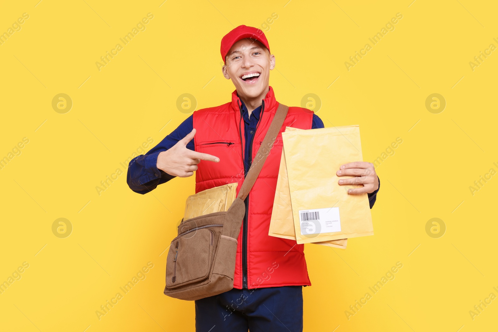 Photo of Happy postman with bag pointing at envelopes on yellow background