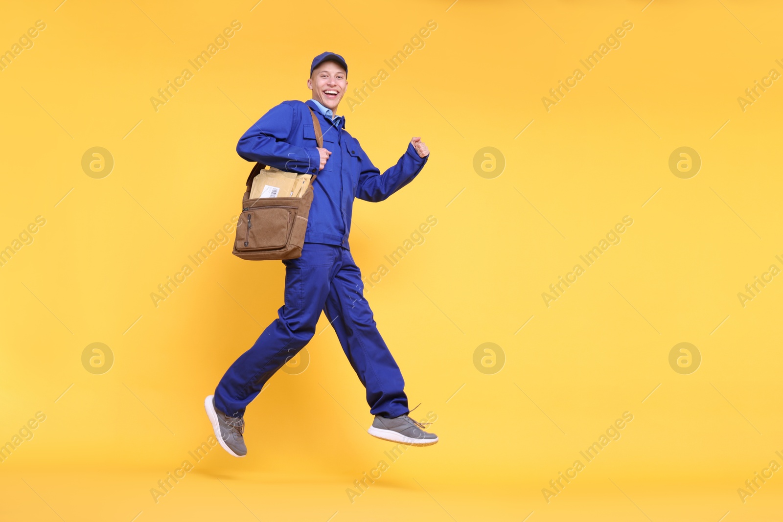 Photo of Happy postman with bag and envelopes jumping on yellow background, low angle view. Space for text