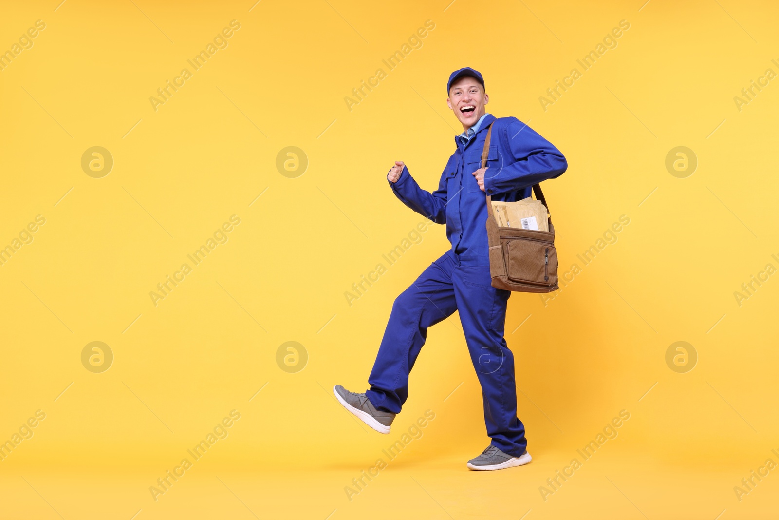 Photo of Happy postman with bag and envelopes on yellow background, low angle view. Space for text