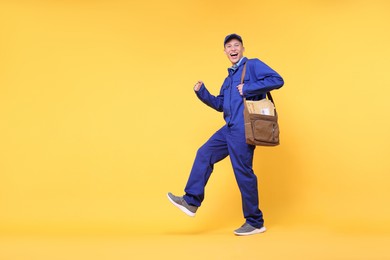 Photo of Happy postman with bag and envelopes on yellow background, low angle view. Space for text