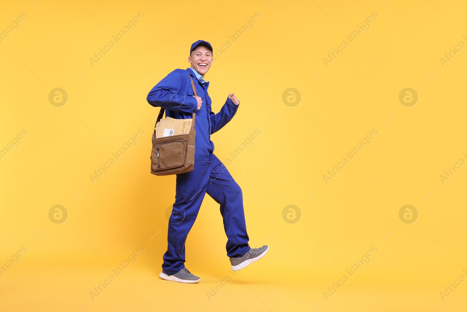 Photo of Happy postman with bag and envelopes on yellow background, low angle view. Space for text