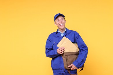 Photo of Happy postman with bag and envelopes on yellow background. Space for text